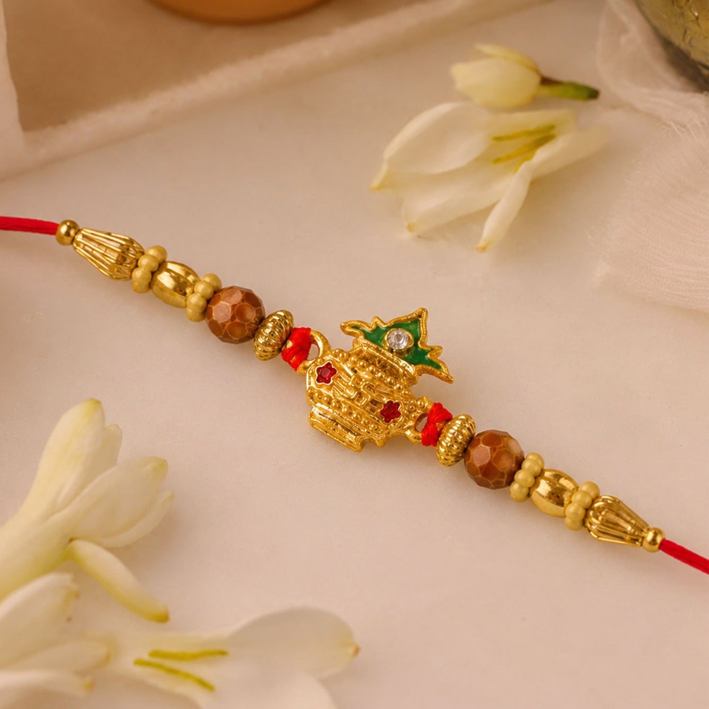 Golden Kalash Rakhi showcasing intricate Moti pearl design and vibrant red thread on a traditional background.
