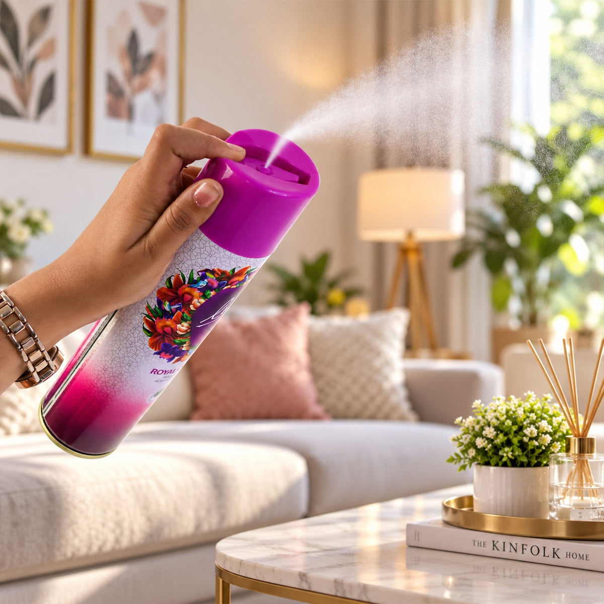 A hand sprays the purple and pink aerosol can, releasing a fine mist into a well-lit living room setting.
