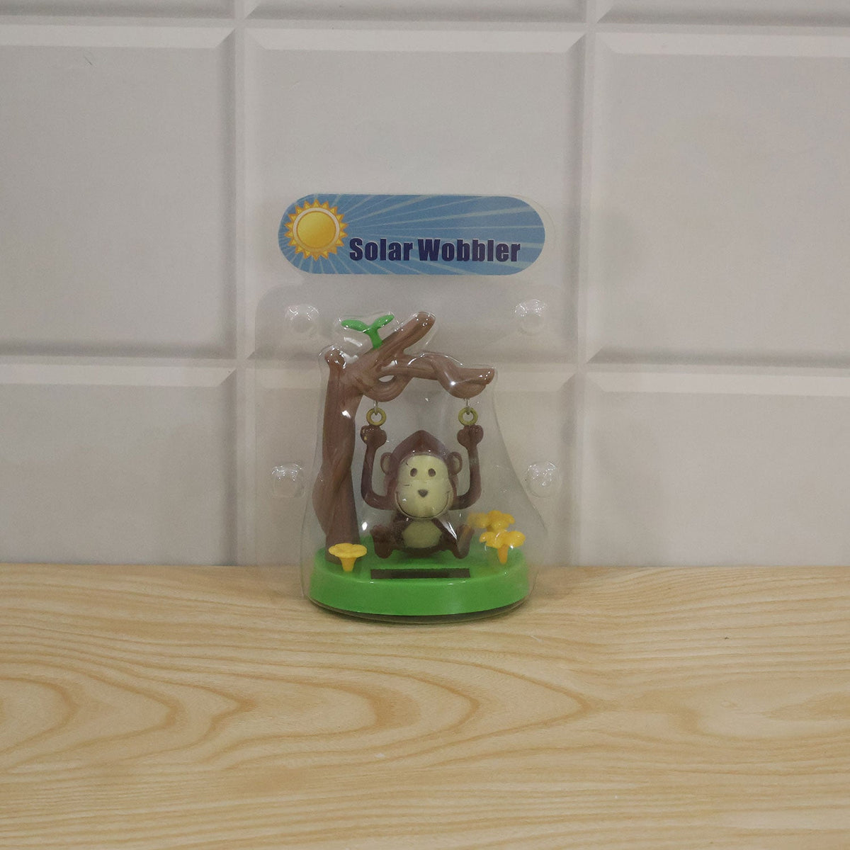 The solar monkey decoration is sealed in clear plastic packaging with a "Solar Wobbler" label, resting on a light wooden