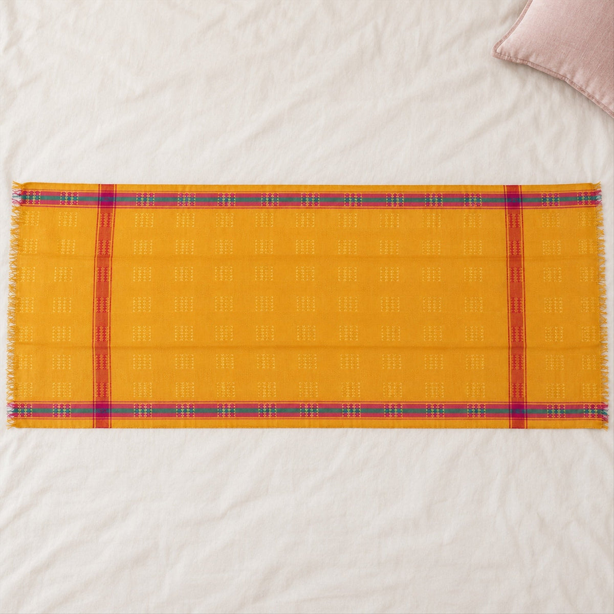 A yellow dupatta with woven square motifs and striped borders in pink and teal is spread on a textured white surface.