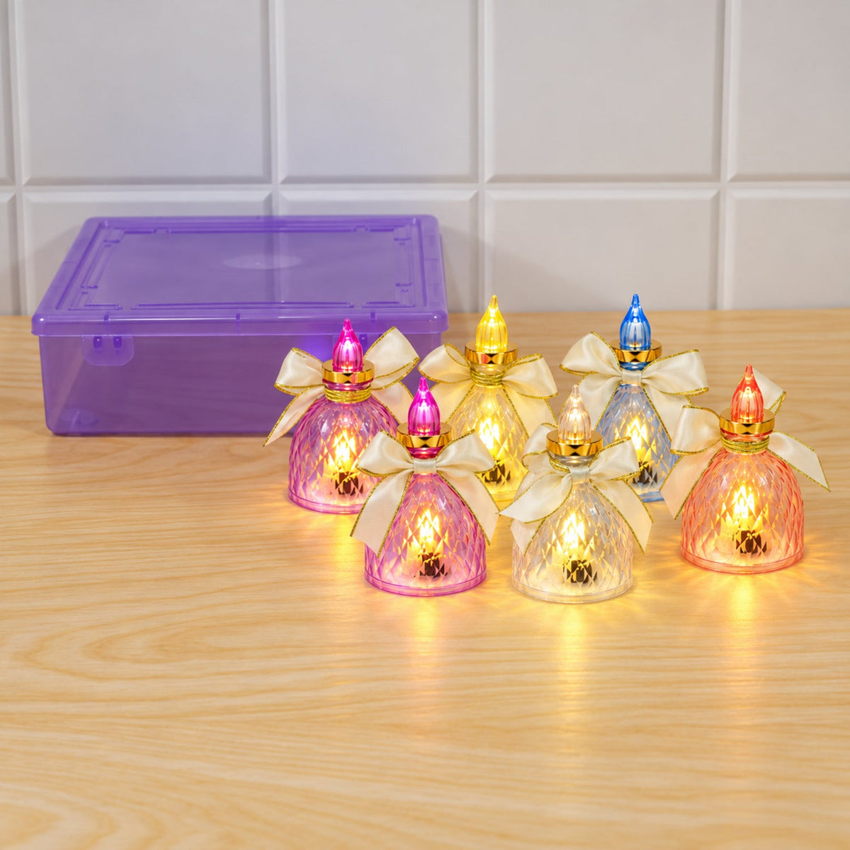 Six colorful LED flameless candles with bows are arranged on a wooden surface next to a purple storage box.