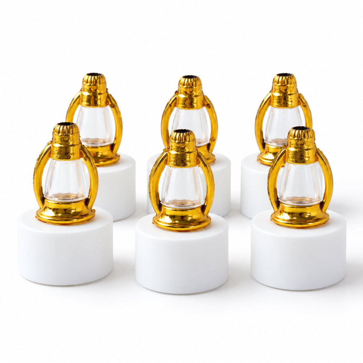 Six unlit miniature lanterns with gold tops and clear glass on white bases are arranged in two rows on a plain white