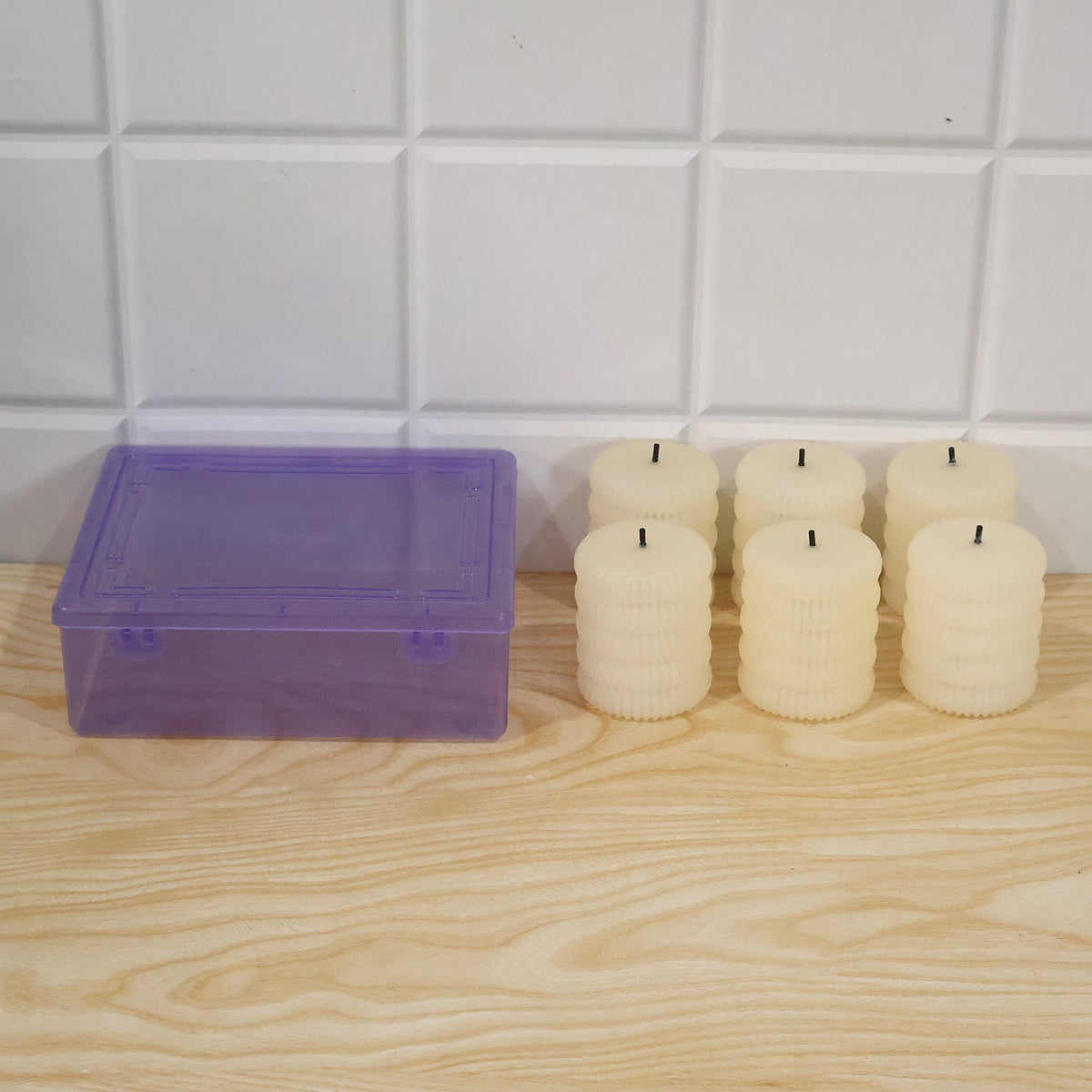 Six unlit cream-colored ribbed flameless LED tealight candles next to a translucent purple storage box.