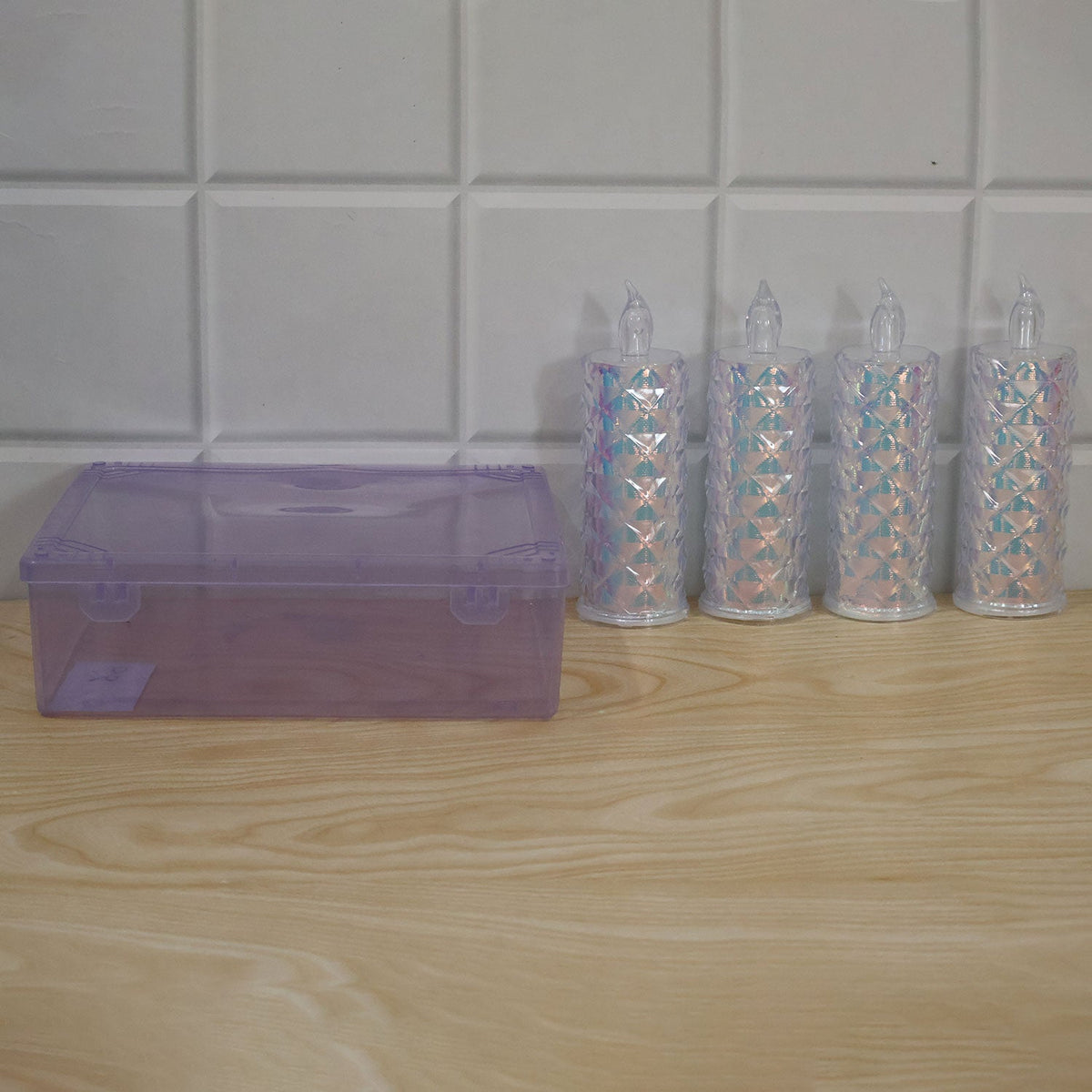 Four unlit crystal LED candles and a closed purple storage box are arranged on a light wooden surface against a white tiled