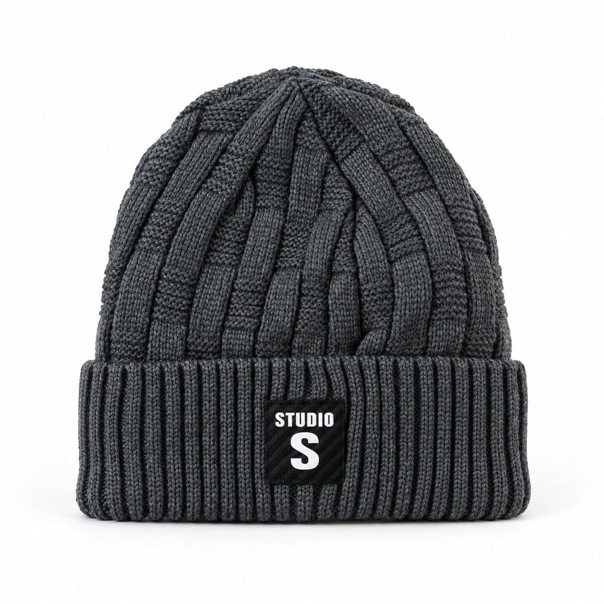 A dark grey cable knit beanie with a ribbed cuff and a black label with "STUDIO S" in white, against a plain white