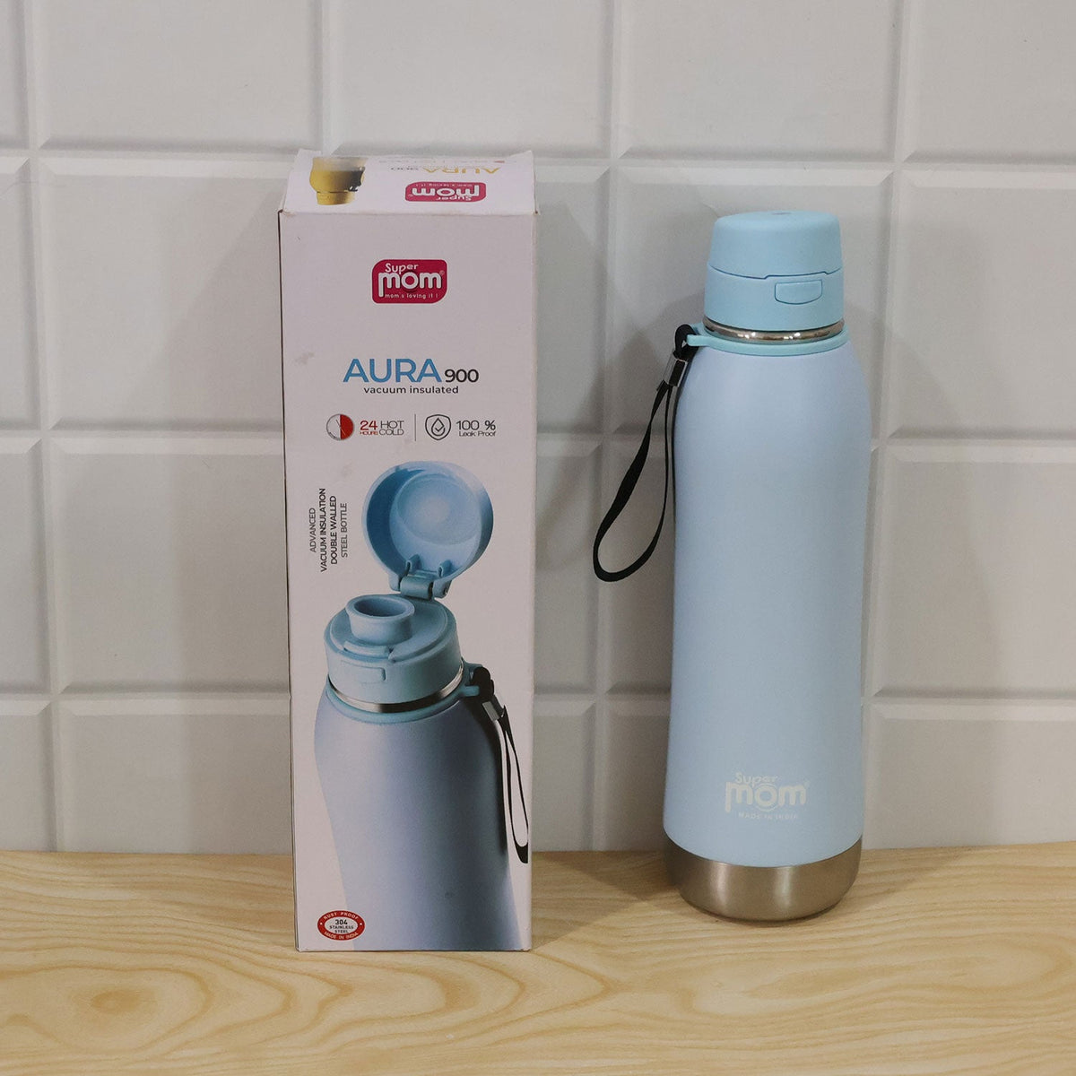 A light blue insulated water bottle with its retail box displayed on a wooden surface against a white tiled wall.