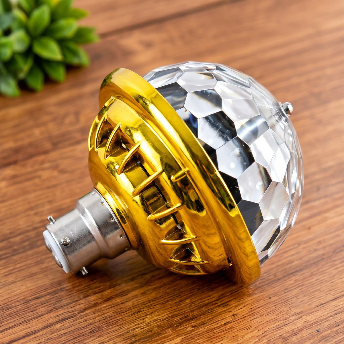 A close-up, angled view of the gold and clear disco bulb with a B22 base resting on a wooden surface.