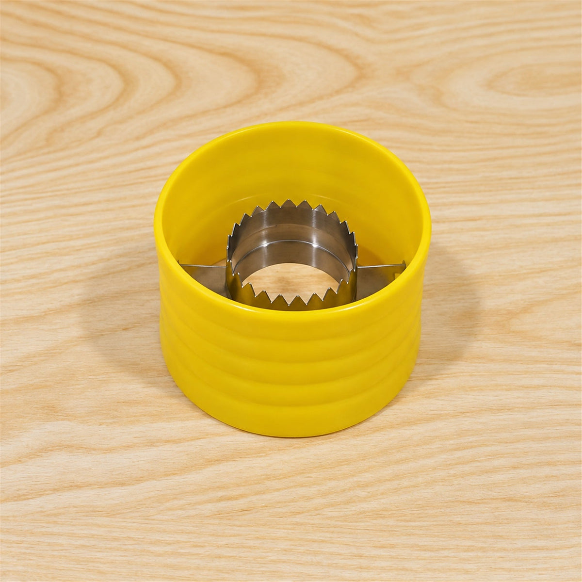 A yellow corn stripper with a silver serrated interior sits centered on a light wooden table.
