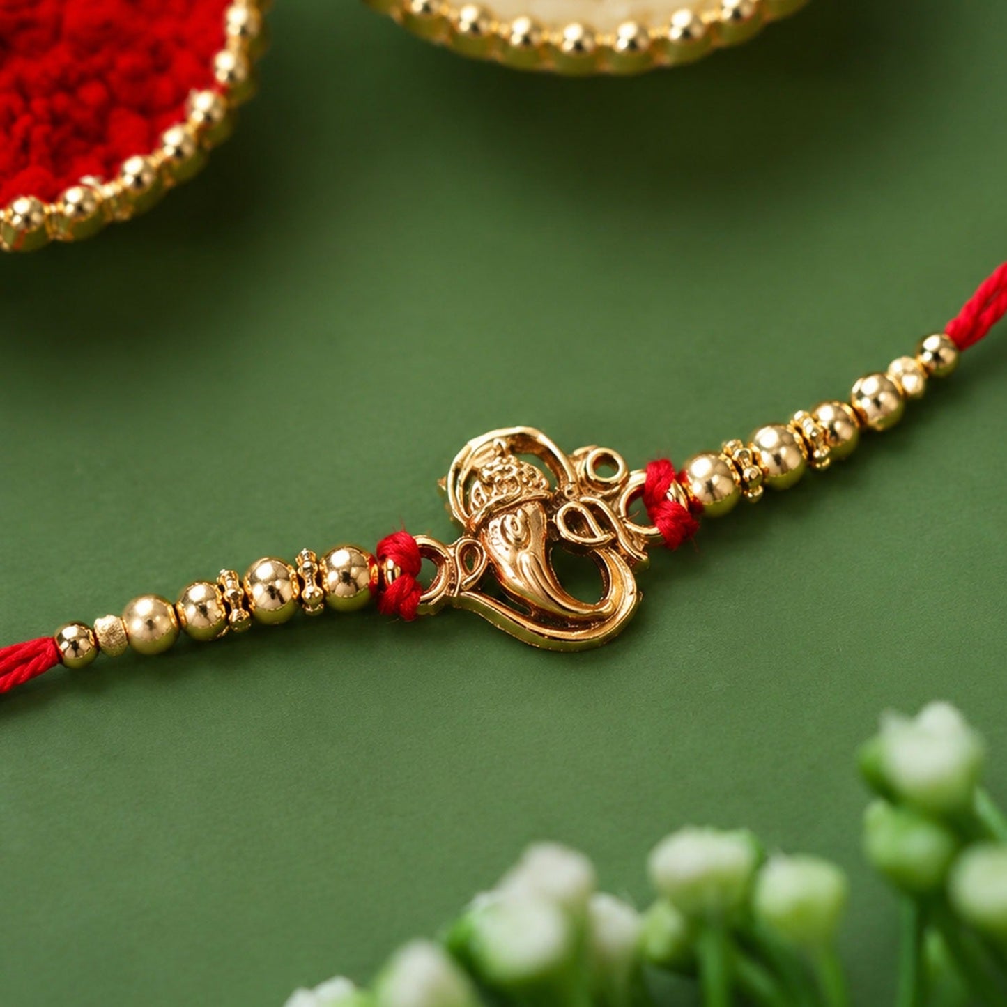 Close-up of a beautiful Ganesha Rakhi with intricate stone work and red thread.