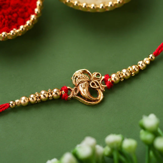 Close-up of a beautiful Ganesha Rakhi with intricate stone work and red thread.