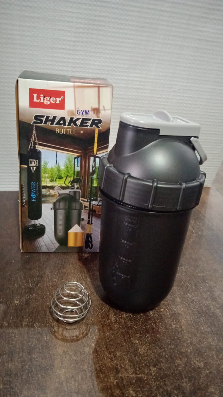 A black shaker bottle and a metal whisk ball sit next to its retail box on a wooden surface.