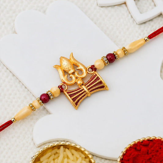 Close-up of Shiva Trishul Rakhi with red and golden bead embellishments symbolizing protection.