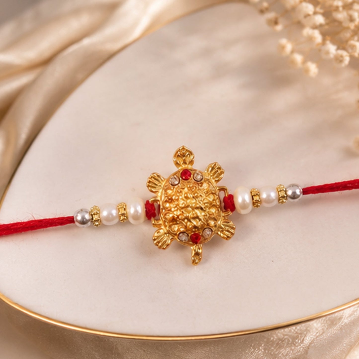 Side view of Turtle Rakhi showing pearl sides and red mauli thread.