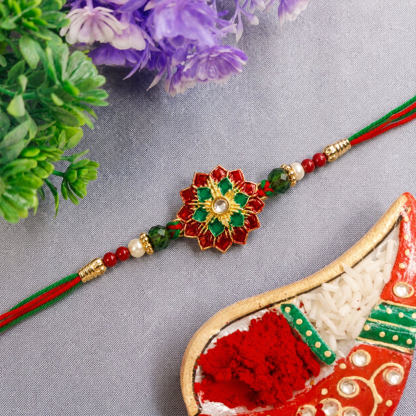 Close-up of floral stonework Rakhi with red & green thread