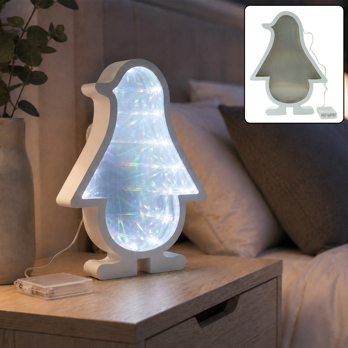 White penguin-shaped infinity mirror light with bright LED illumination, sitting on a wooden nightstand next to a green