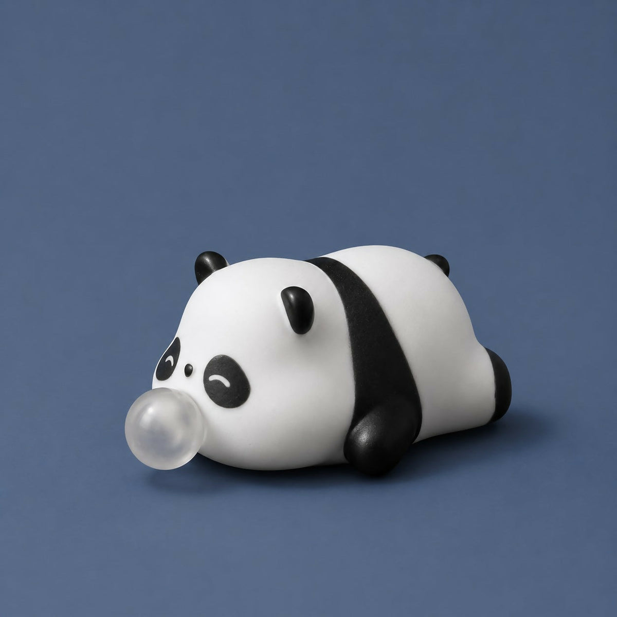 A cute white and black panda squeeze toy, lying down with a clear bubble emerging from its mouth, is centered against a