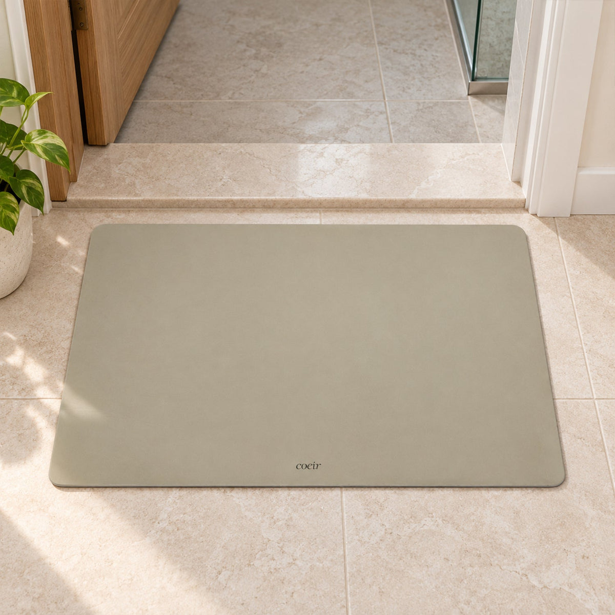 A light beige rectangular floor mat with rounded corners sits on tiled flooring near a doorway.