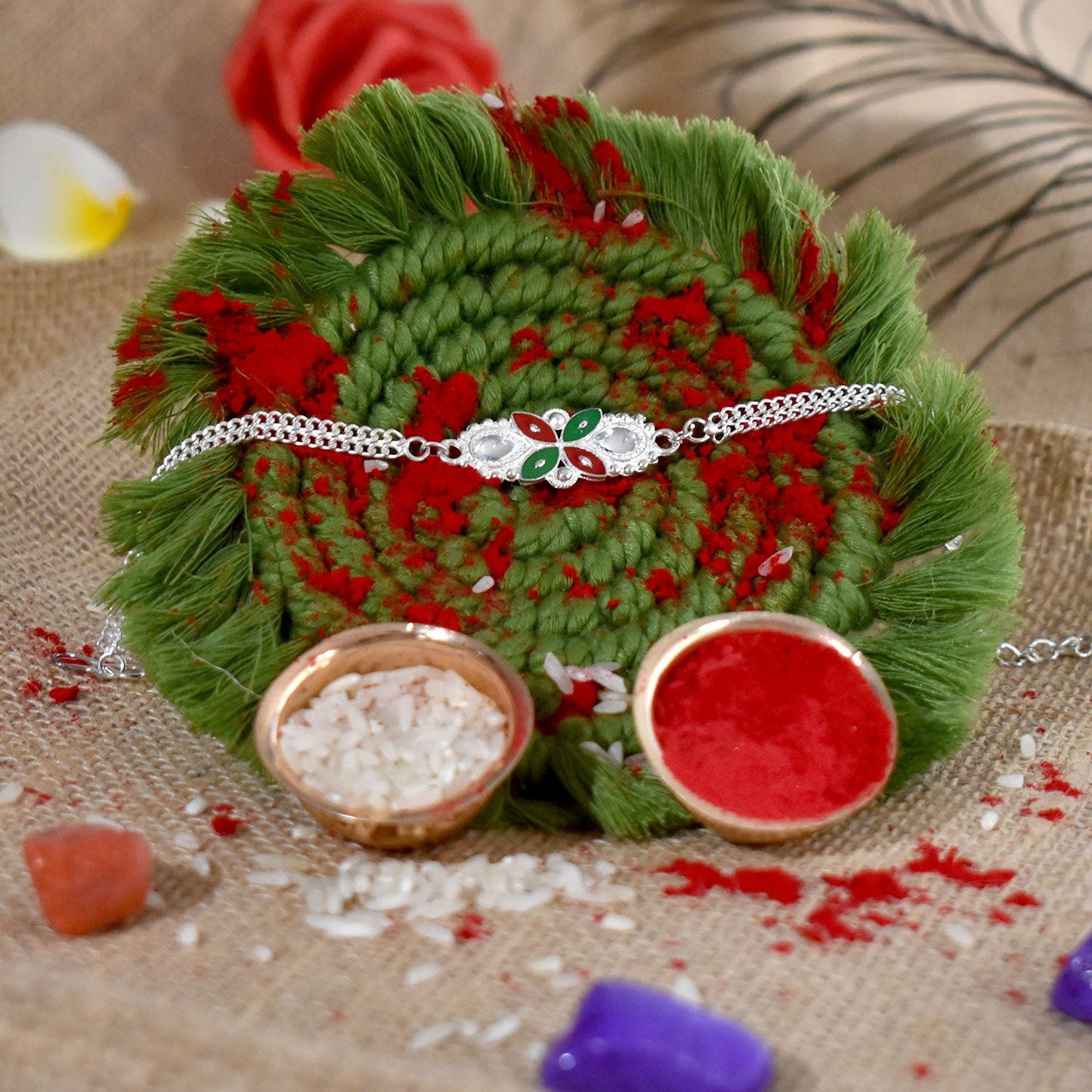 Close-up view of the intricate red and green enamel floral pattern on the traditional Rakhi.
