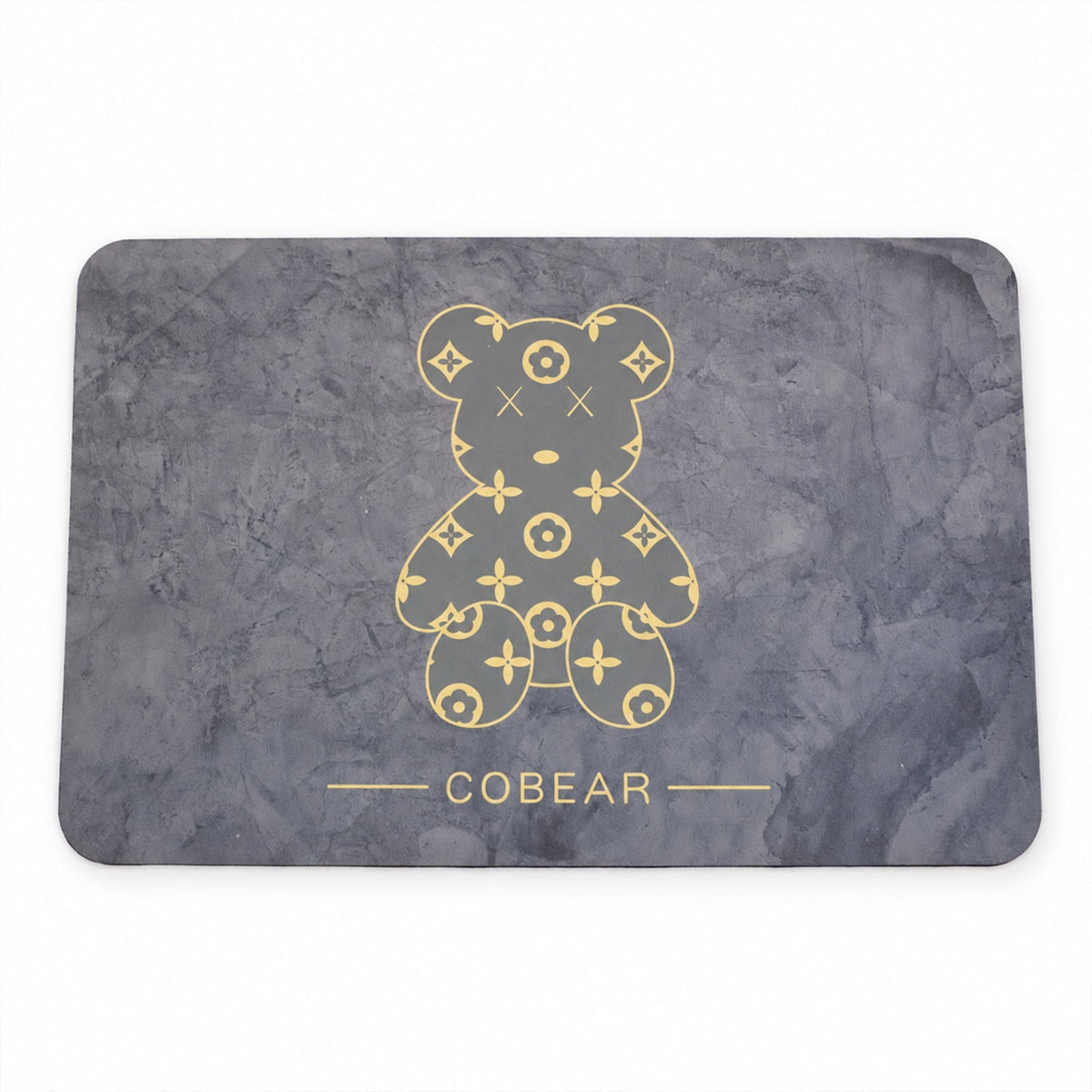 A plain overhead view of the grey rectangular bath mat with a golden patterned bear and 'COBEAR' text.