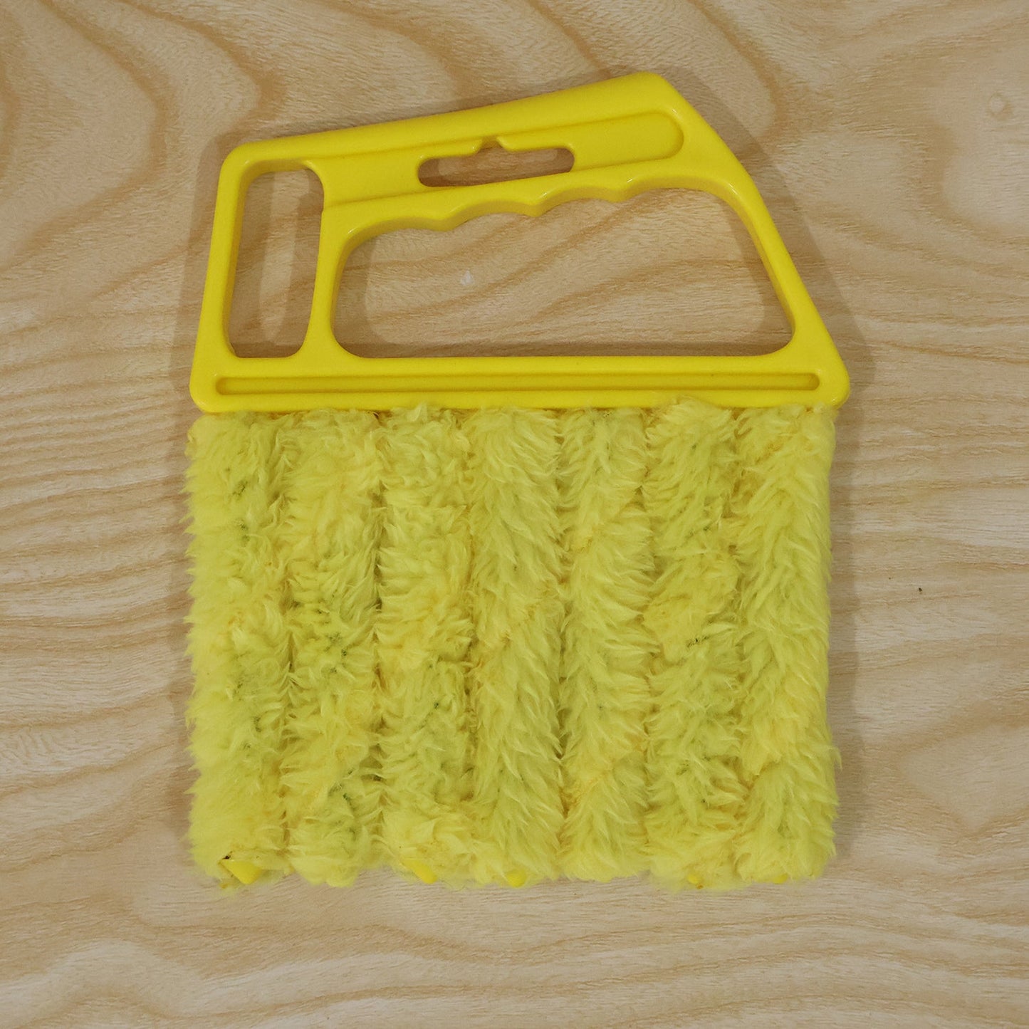A yellow microfiber blind cleaner with a plastic handle and five microfiber cleaning fingers, on a light wooden surface.