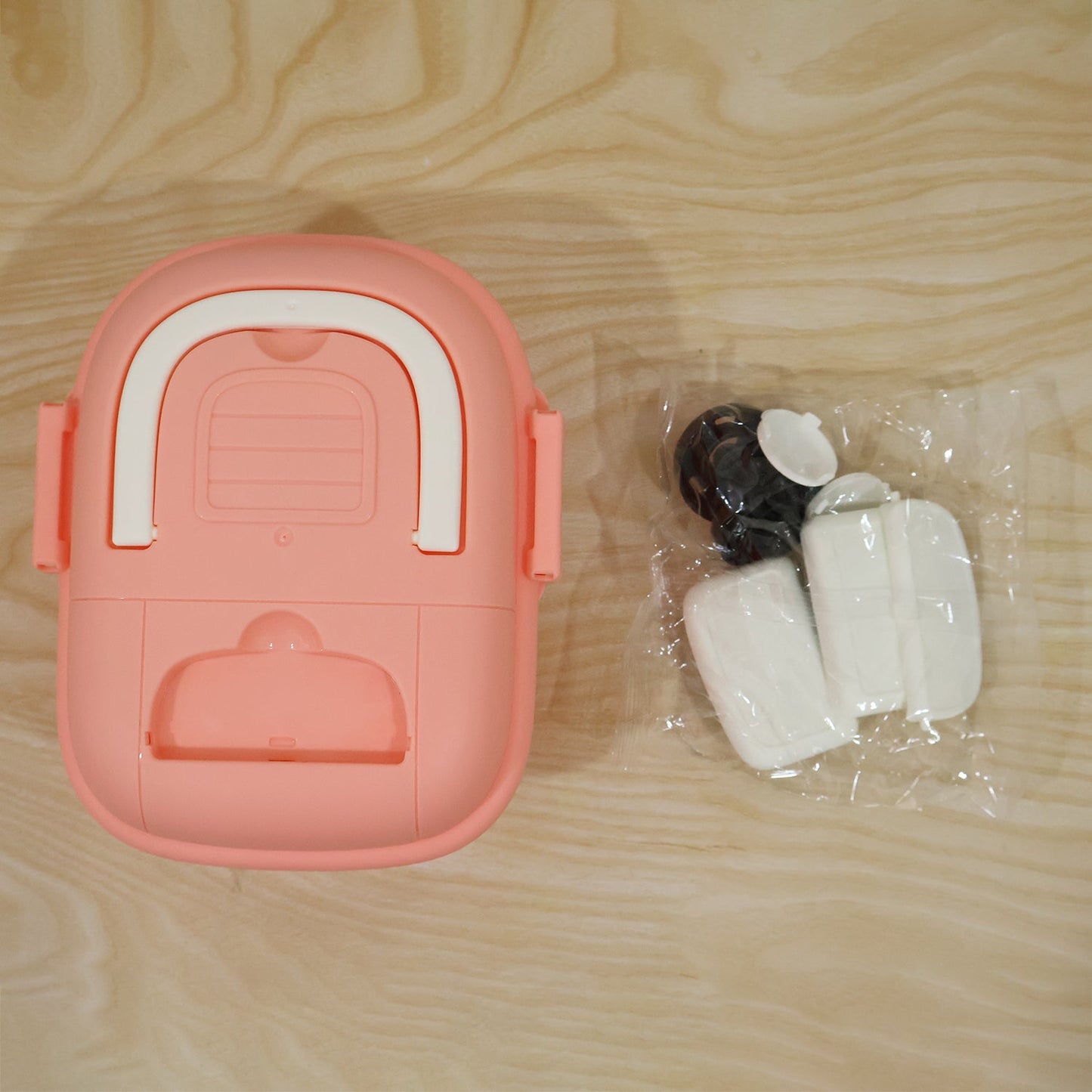 The underside of the pink fire truck toy storage box lid is shown next to a plastic bag containing white and black parts.