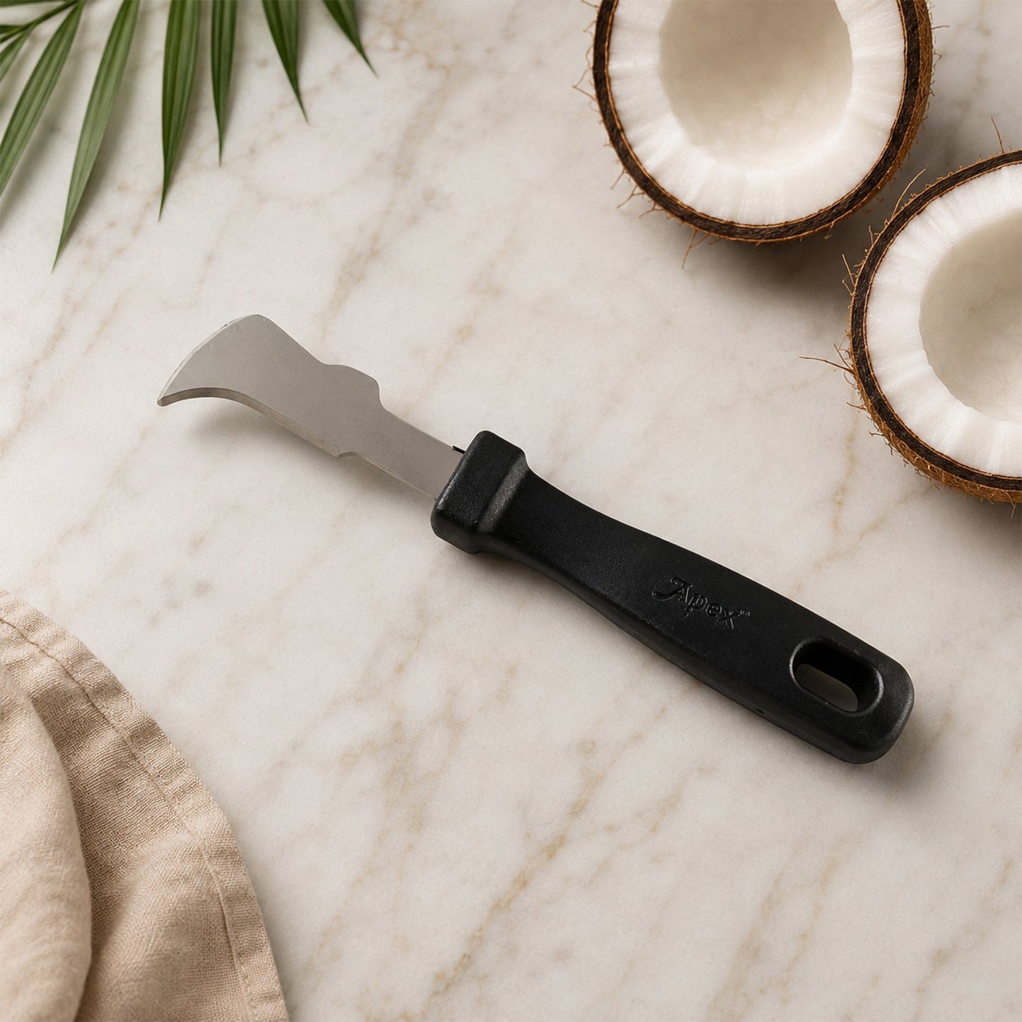 The Apex coconut meat removal tool with a black handle and silver blade lies on a marble surface with coconut halves.