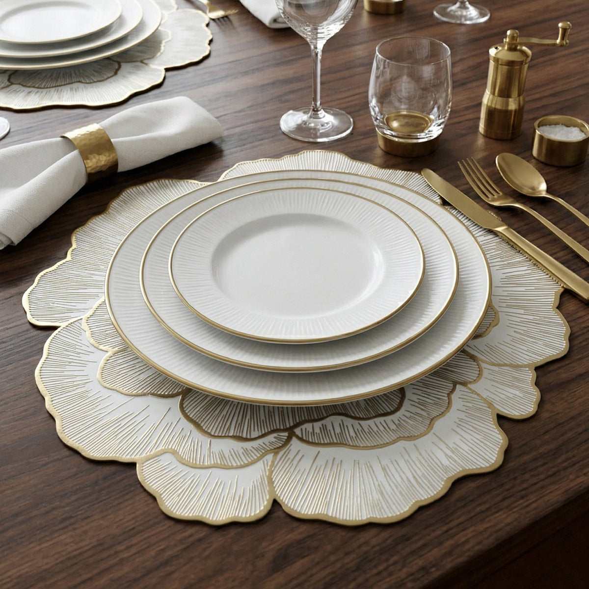 A table setting with a white and gold floral placemat, stacked plates, and golden utensils.