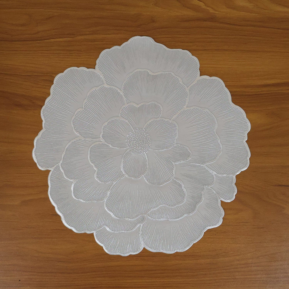 A top-down view of a silver floral placemat with intricate petal details on a wooden table.