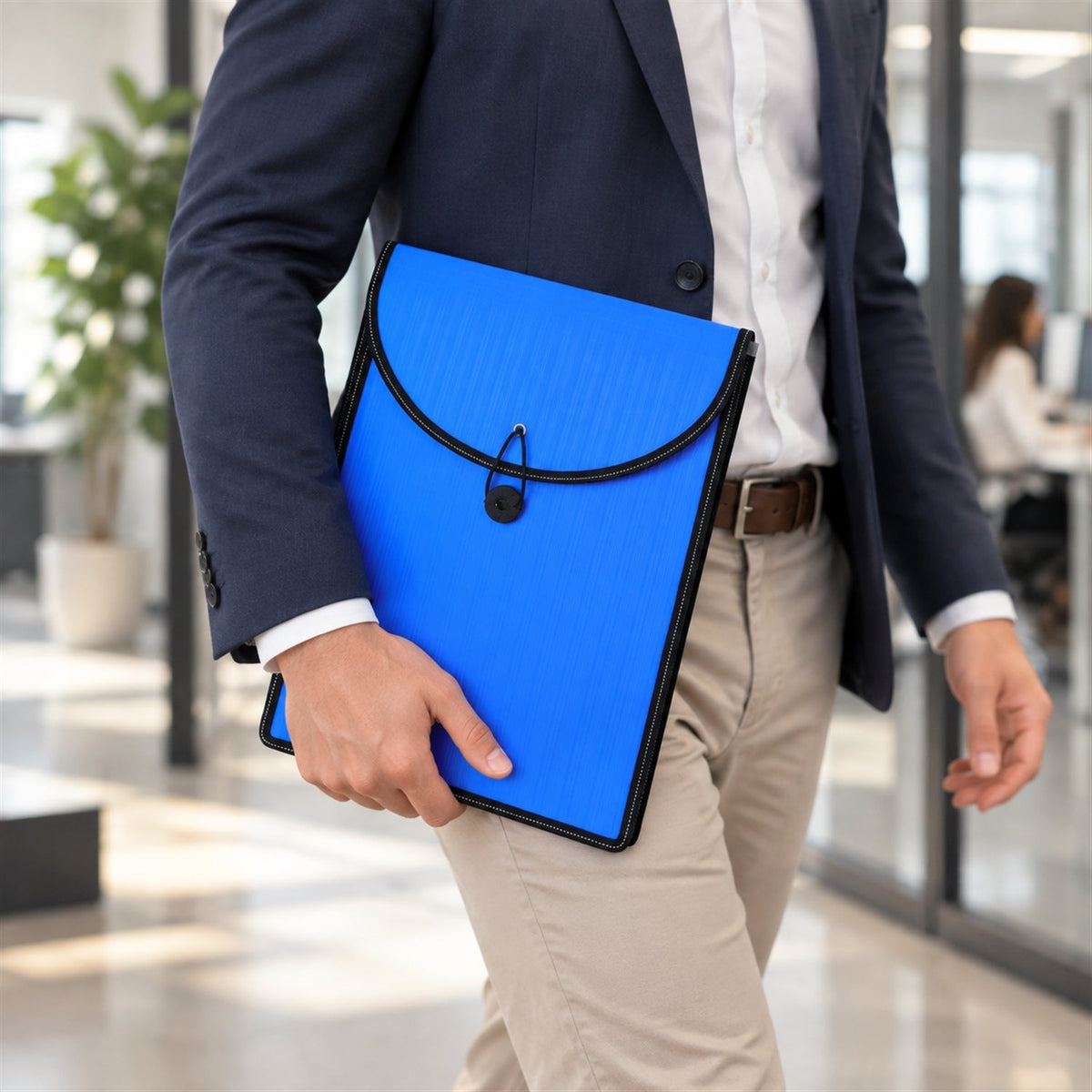A person in business attire walking while holding a blue plastic document folder with a black elastic closure.