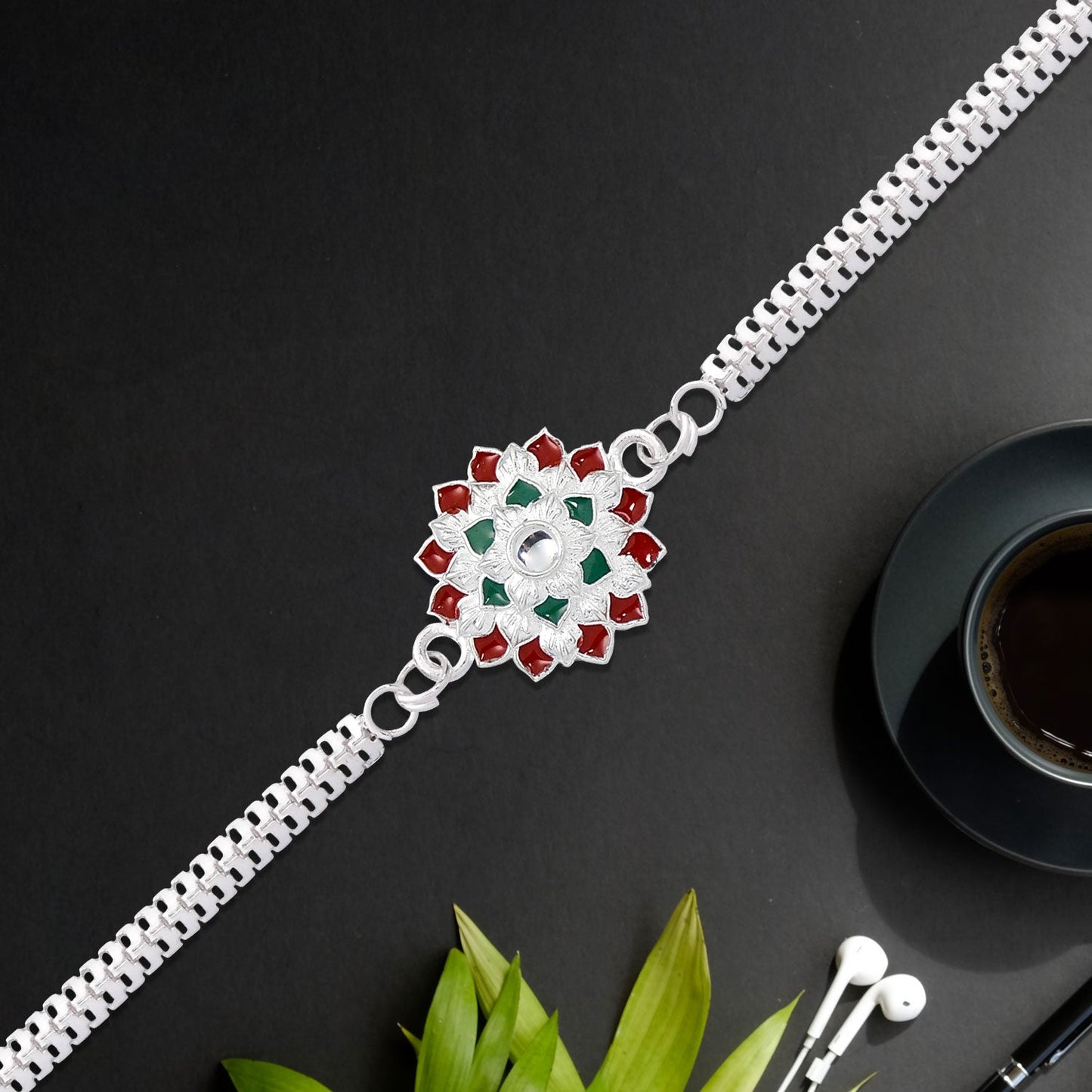 Intricate design of a traditional Silver Chain Rakhi with red and green elements.