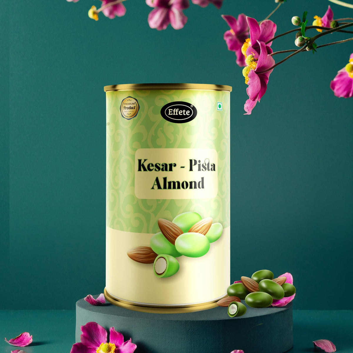 A Kesar Pista Almond tin rests on a dark green pedestal with pink flowers scattered around.