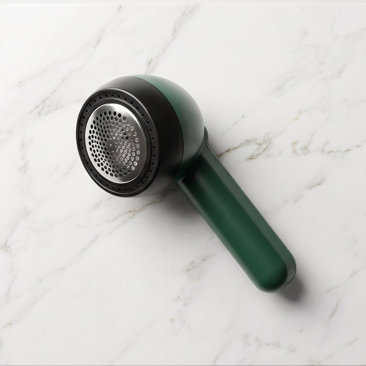 A dark green and black lint remover with a silver mesh head rests on a white marble surface.