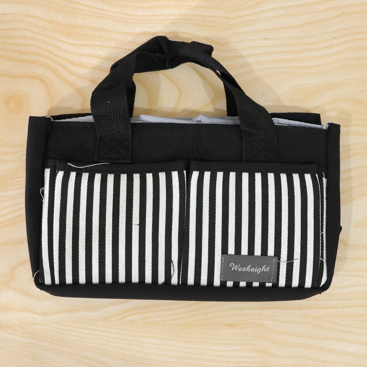 A black and white striped organizer bag caddy with handles is displayed flat on a light wooden surface.