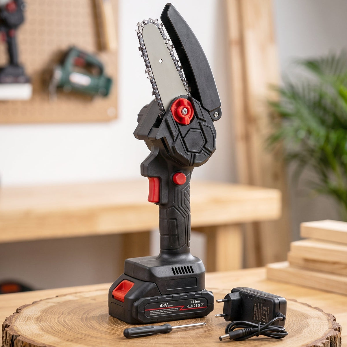 Gloved hand holding a black and red mini chainsaw, cutting a tree branch in a sunny garden.