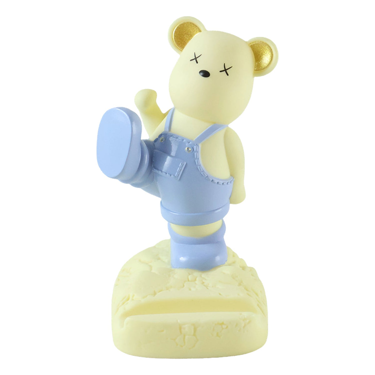 A light yellow bear phone stand wearing blue overalls, standing on a textured base, against a white background.