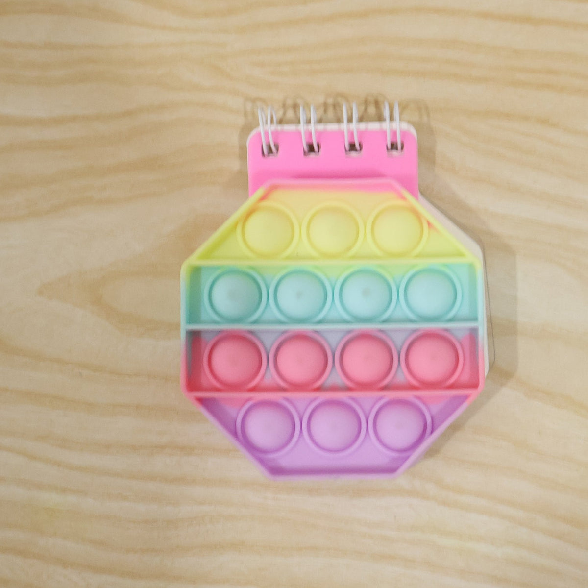 A pastel hexagon pop it fidget notebook with a pink spiral binding on a light wooden surface.