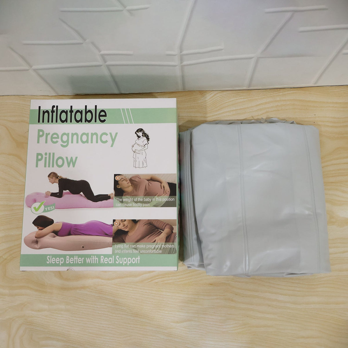 A white box for an inflatable pregnancy pillow is next to a folded grey inflatable mat on a wooden surface.