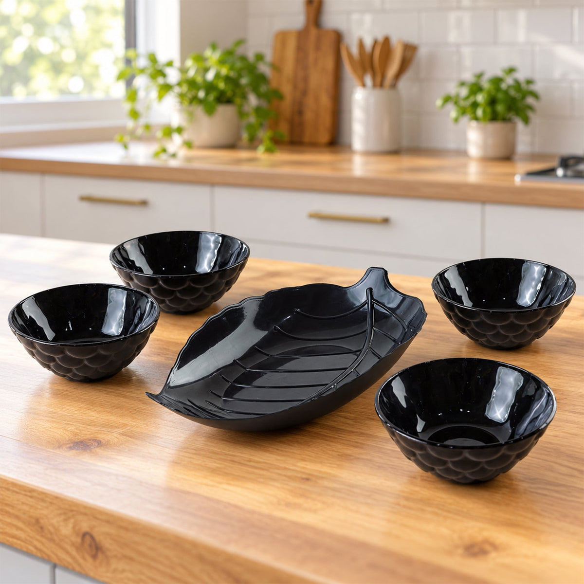 A black leaf-shaped platter and four small black bowls are neatly arranged on a light wooden kitchen counter.