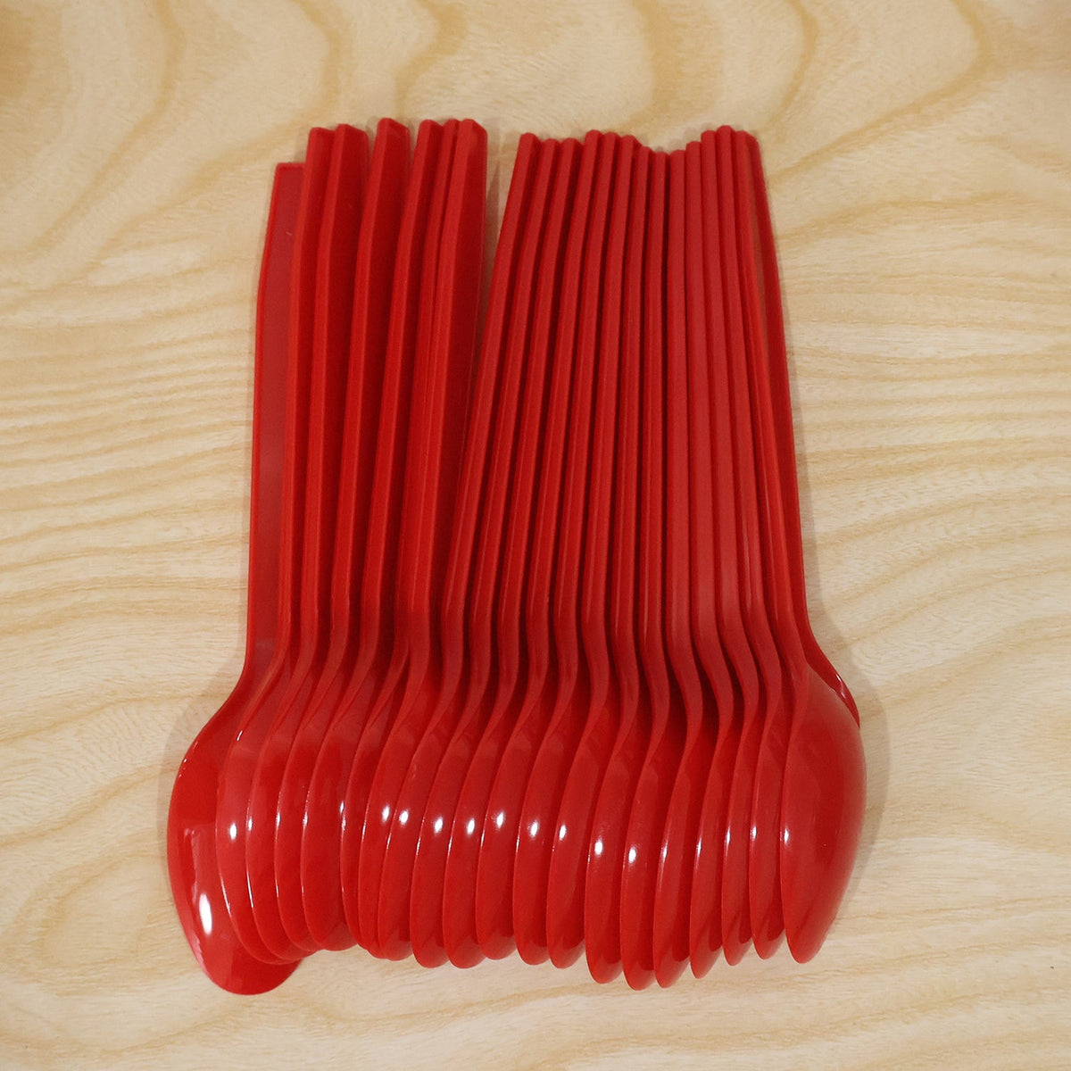 A stack of red plastic spoons, fanned out, on a light wooden surface.