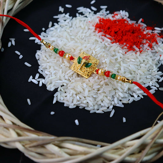 Golden Ganpati Rakhi featuring red and green beads and delicate enamel detailing