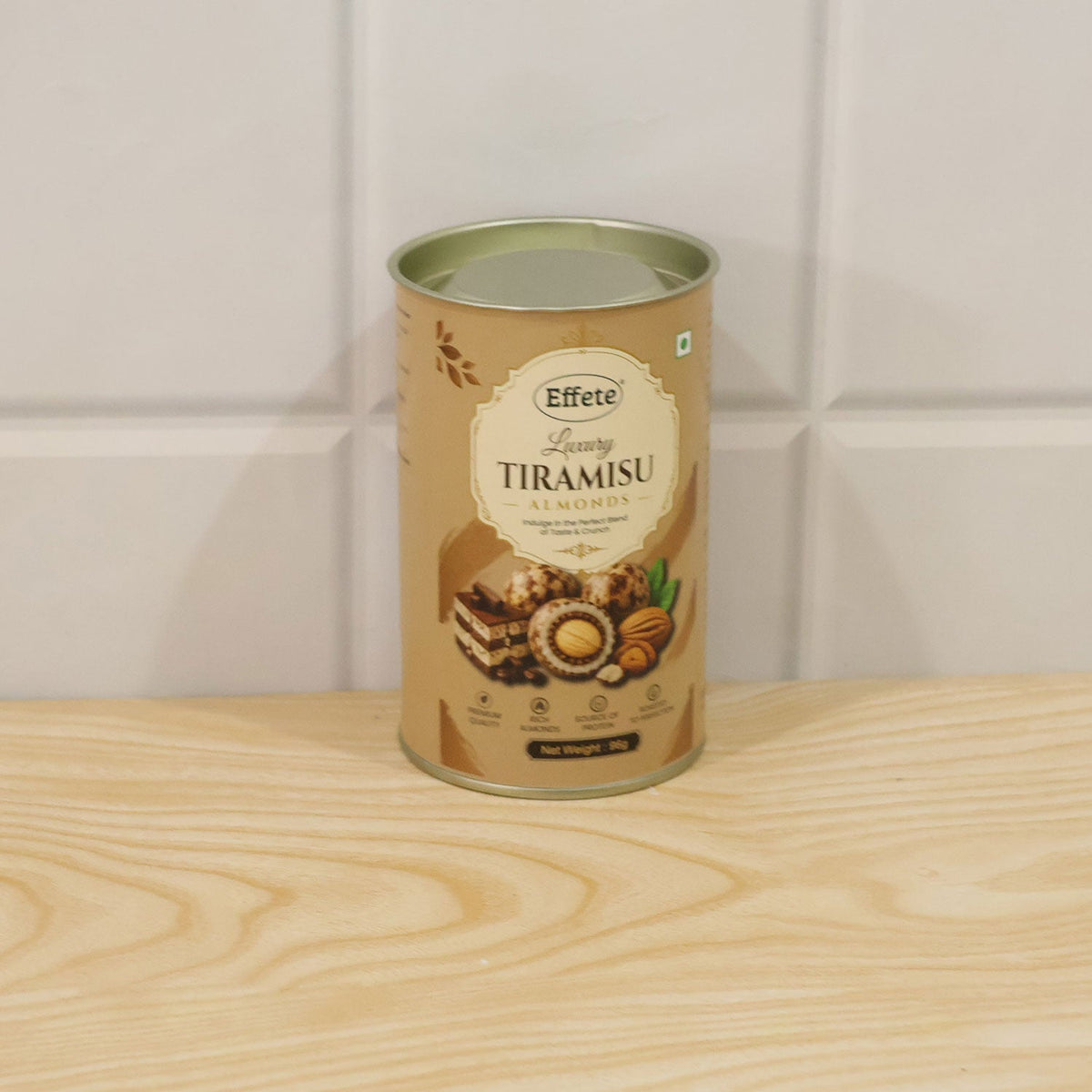 A single Effete Luxury Tiramisu Almonds canister stands upright on a light wooden surface against white tiled wall.