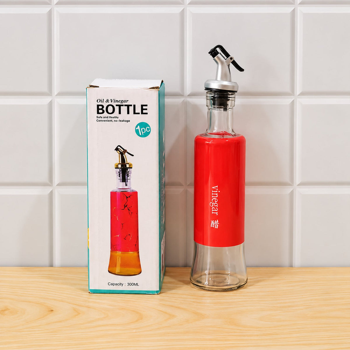 A red-sleeved glass bottle with a pour spout stands next to its white and teal packaging box on a wooden surface.