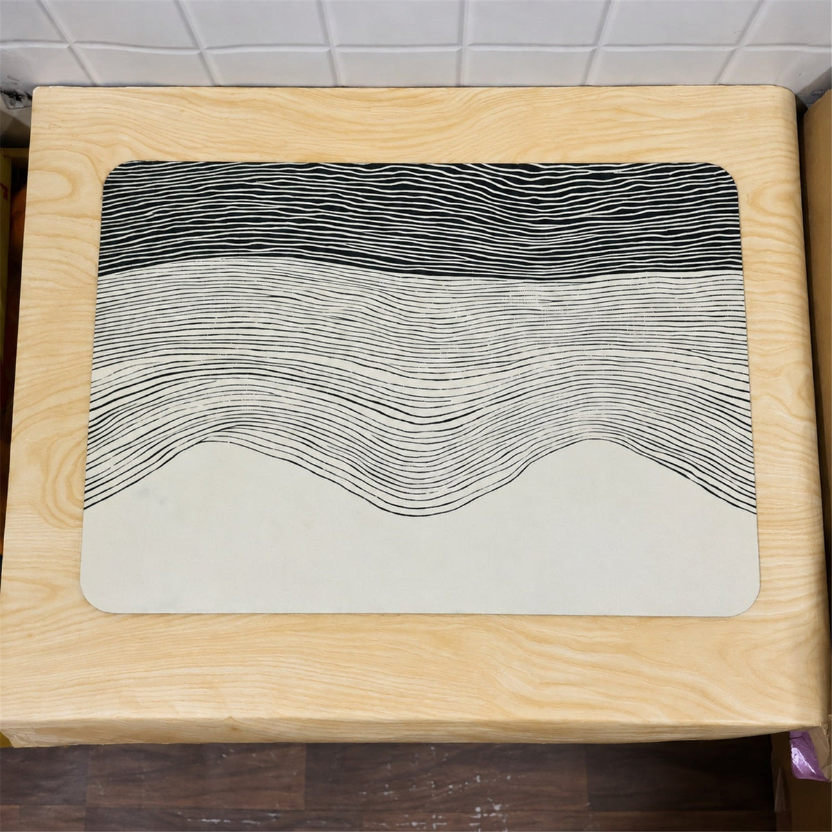 A rectangular mat with a black and white wavy line design rests on a light wooden surface.