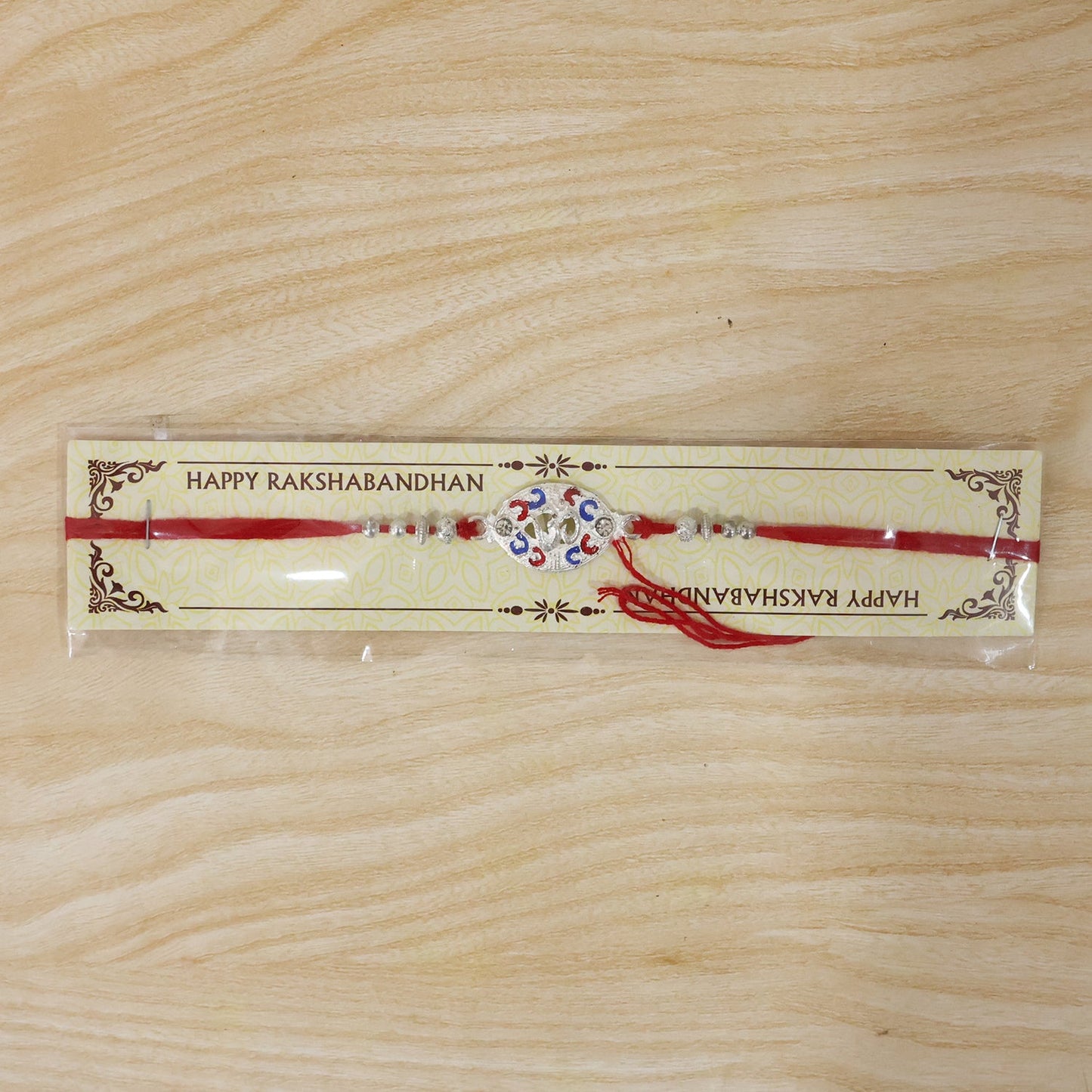 Neatly finished silver Om rakhi with vibrant accents and red thread