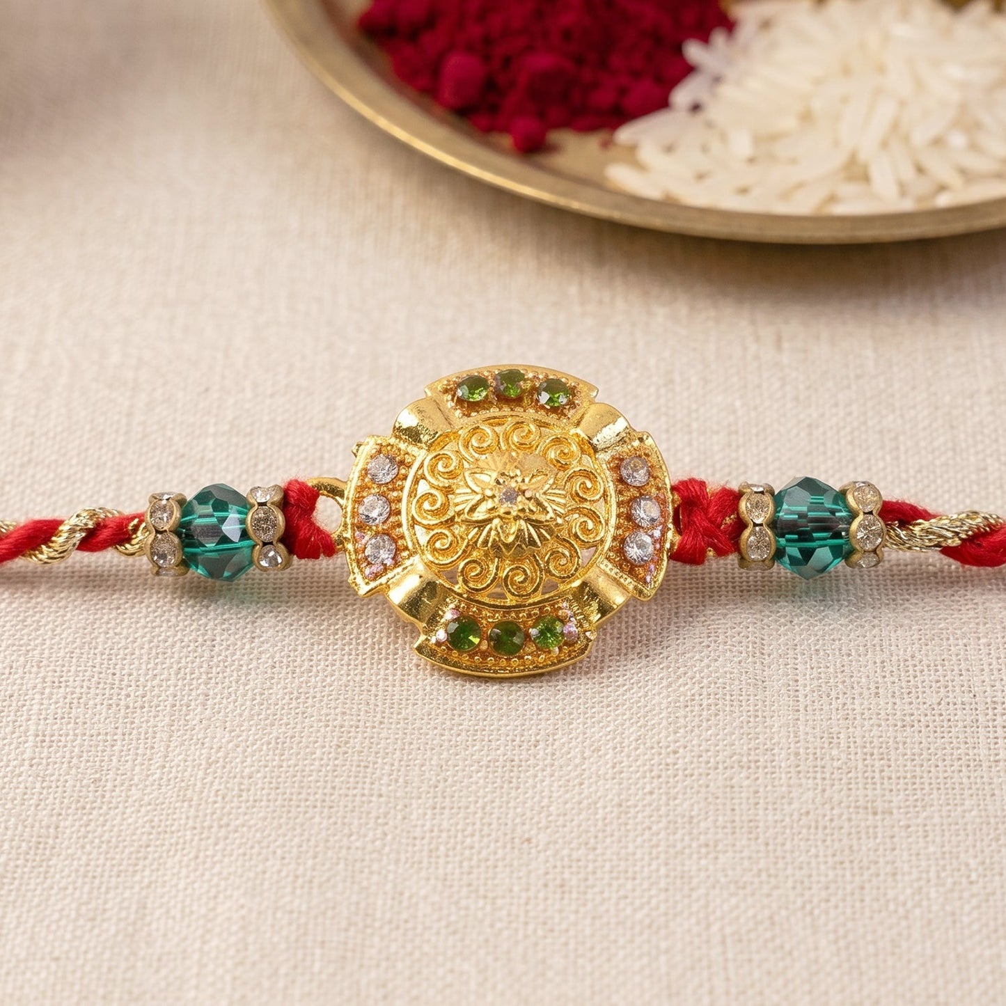 Close-up of green stone beads on a traditional gold floral Rakhi.