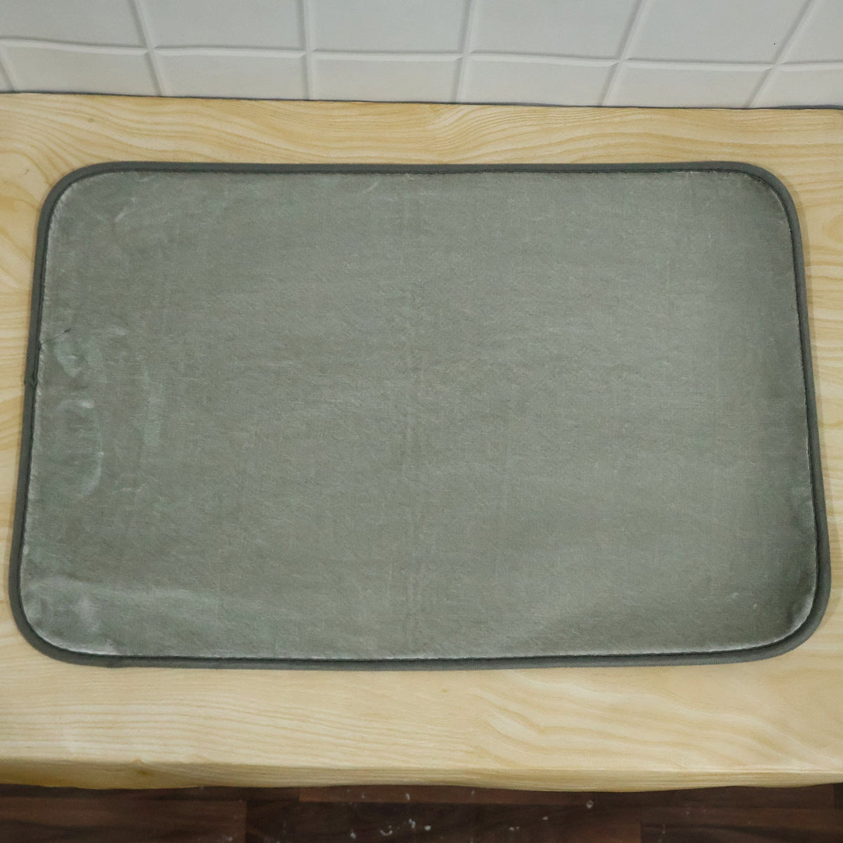 A grey rectangular mat with a dark border sitting on a light wooden surface.