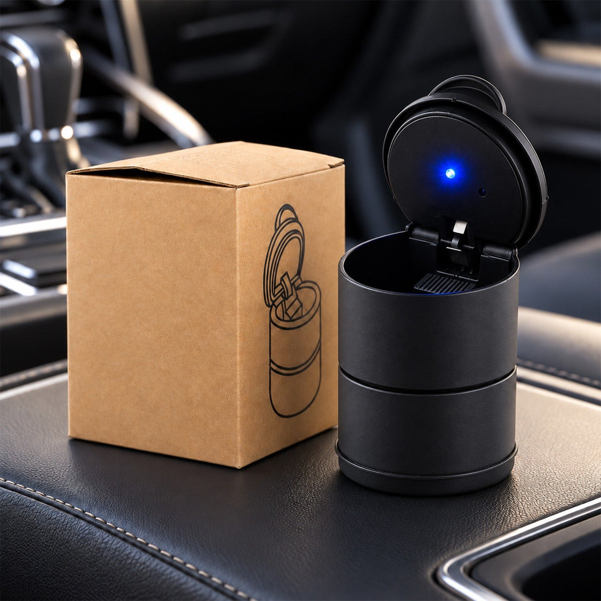 A black car ashtray with a blue LED light open next to its brown cardboard packaging inside a vehicle.