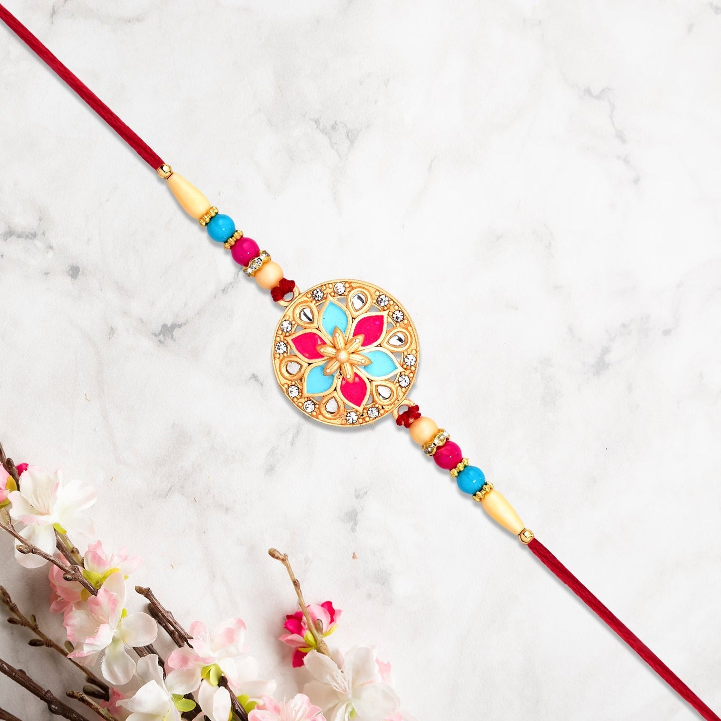 Artistic floral rakhi with pink and blue enamel accents and fine beaded thread