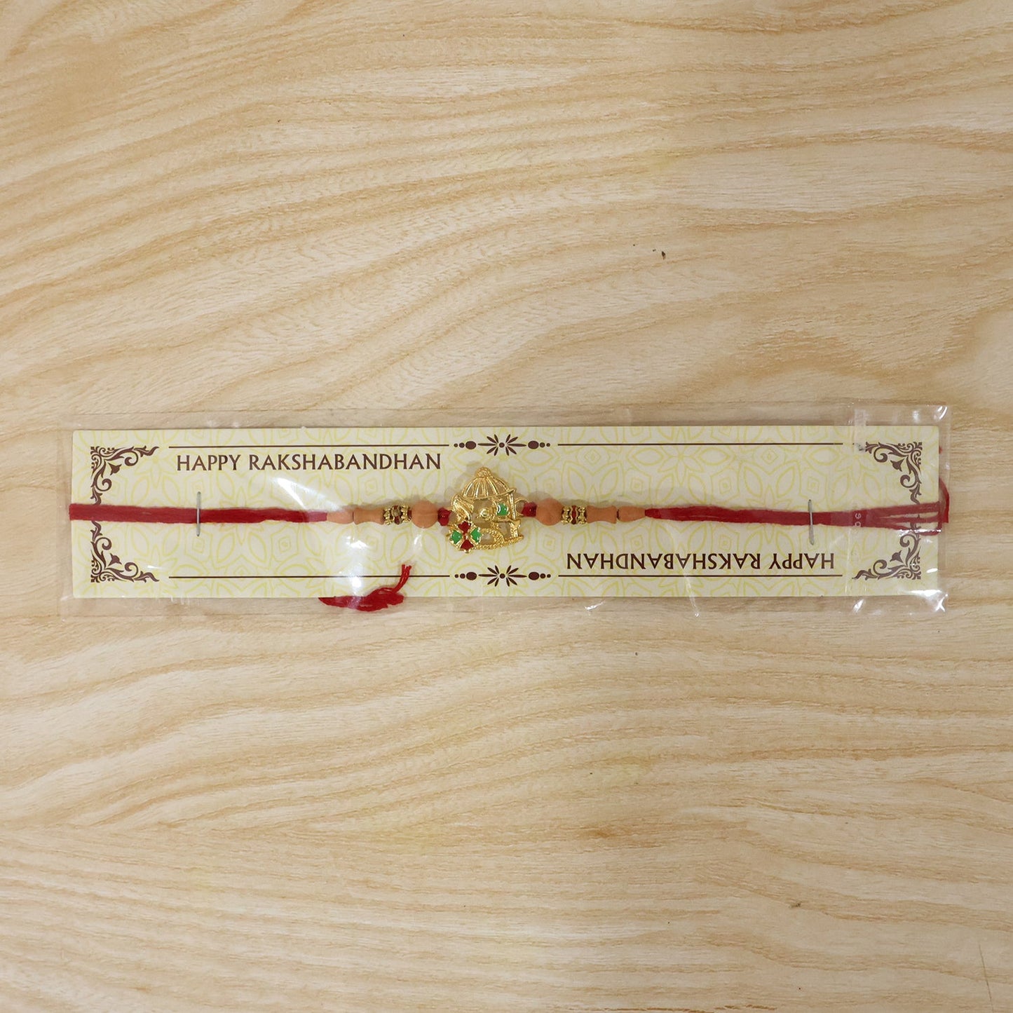 Designer Rakhi featuring golden bow and arrow centerpiece with red beads