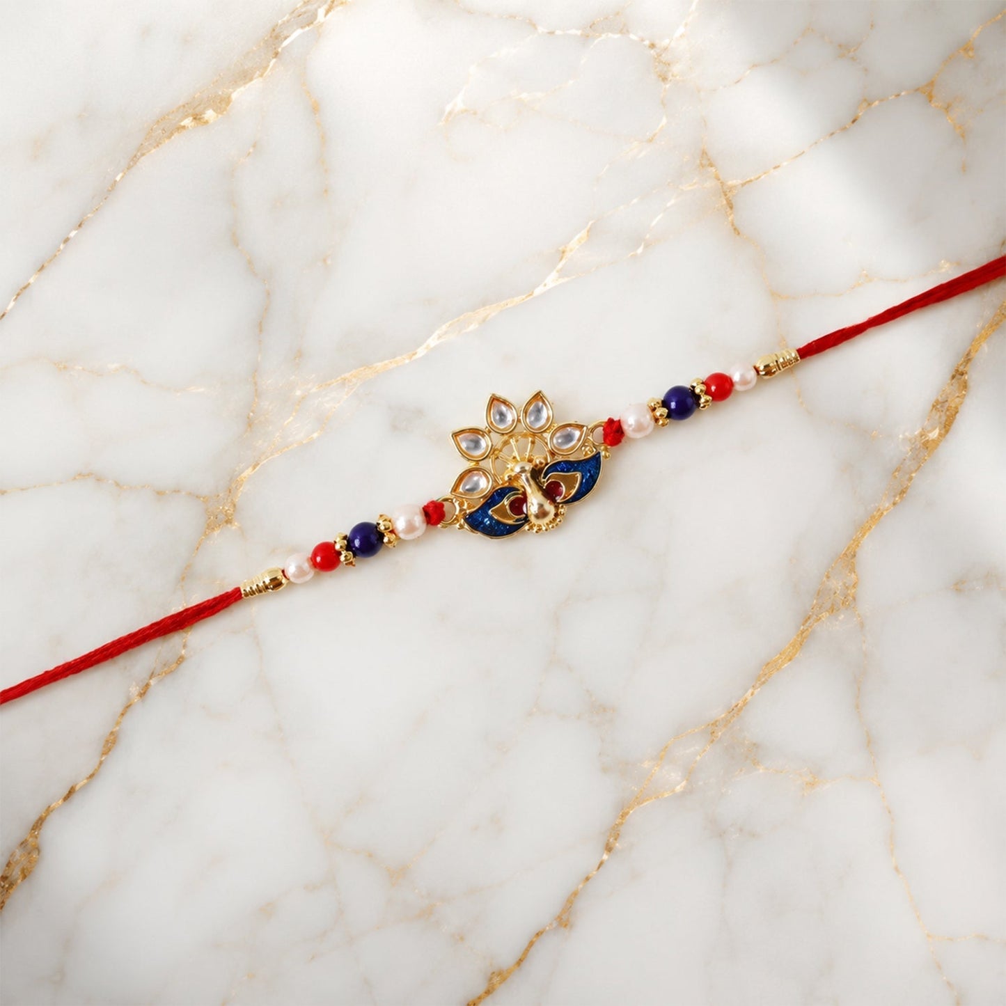 Peacock rakhi displayed on hand featuring vibrant red thread